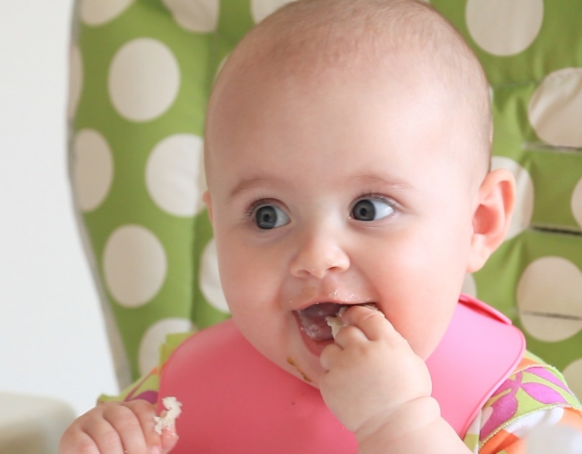 Baby lifting pureed food to mouth and smiling