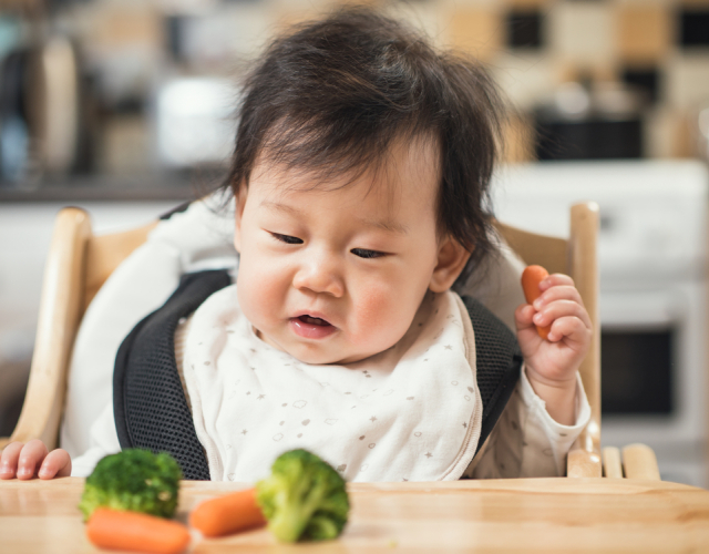 Baby in high chair starting taste journey with broccoli and carrot