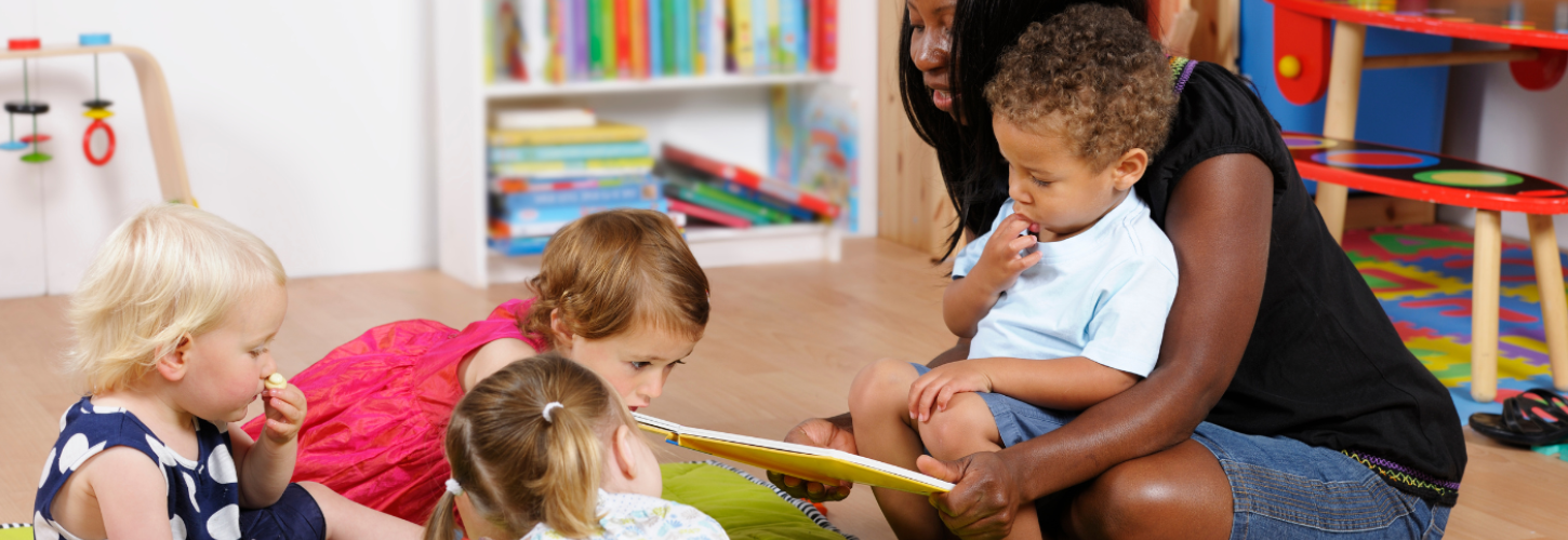 black woman childminder sitting with four kids reading a book